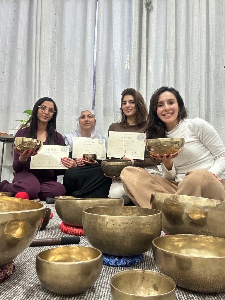 أربع مشاركات جالسات على السجاد وسط طاسات تبتية متنوعة الأحجام مع الشهادات