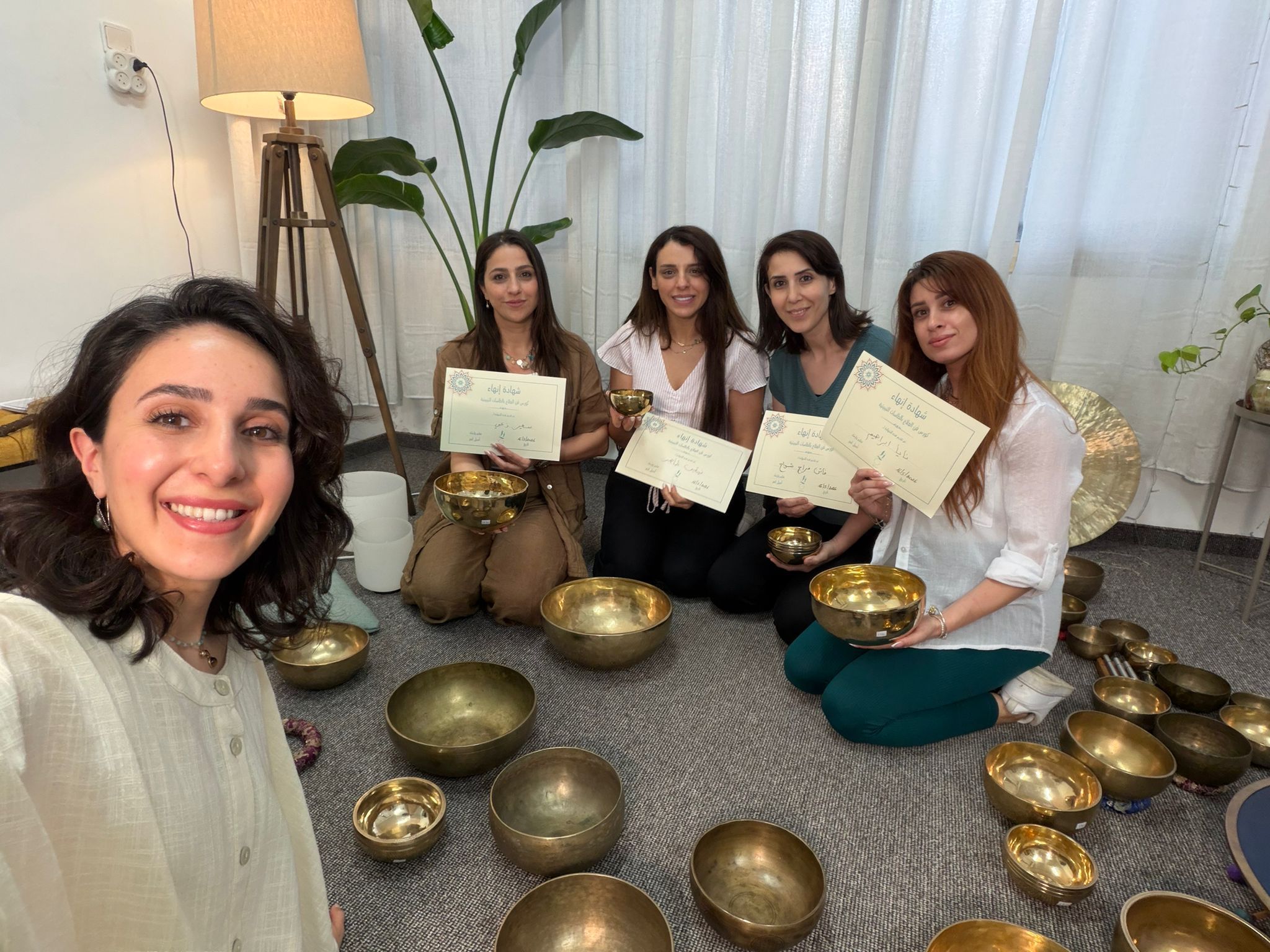 صورة جماعية للمشاركات مع شهادات الإنهاء وطاسات تبتية في الاستوديو